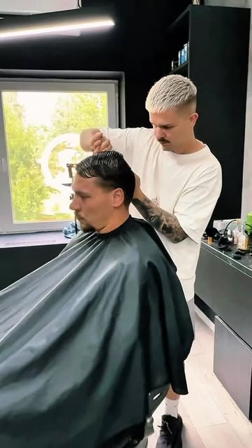 Barber strihá zákazníka pri okne